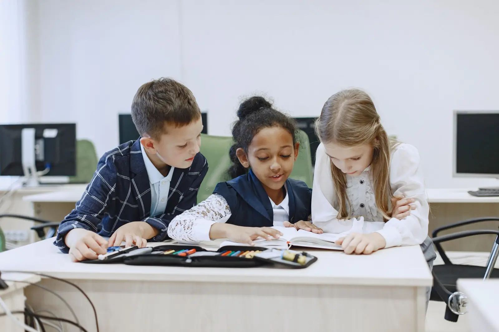 Three children working together on a book at a classroom desk