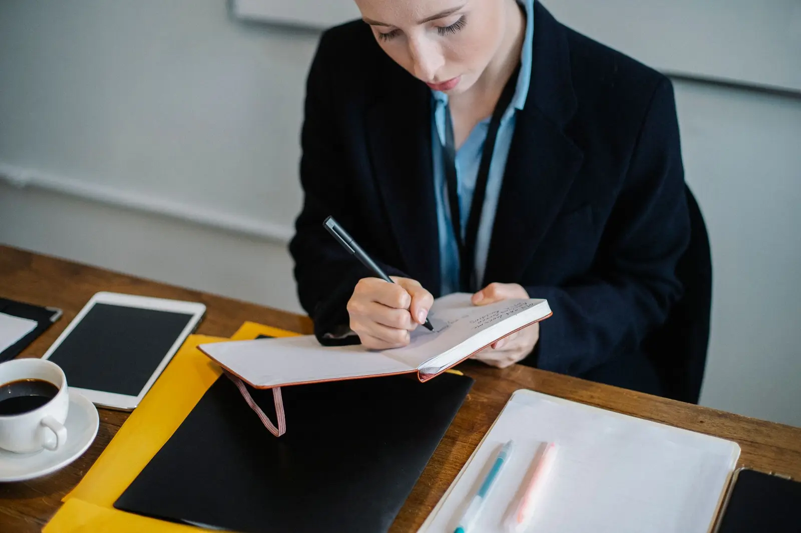 A woman writing notes in a planner at a desk with a tablet and coffee