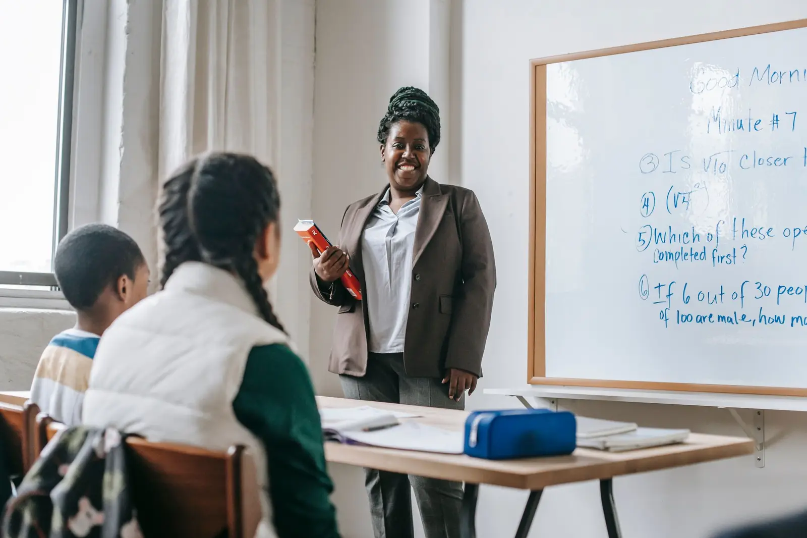 A smiling teacher standing by a whiteboard talking to pupils