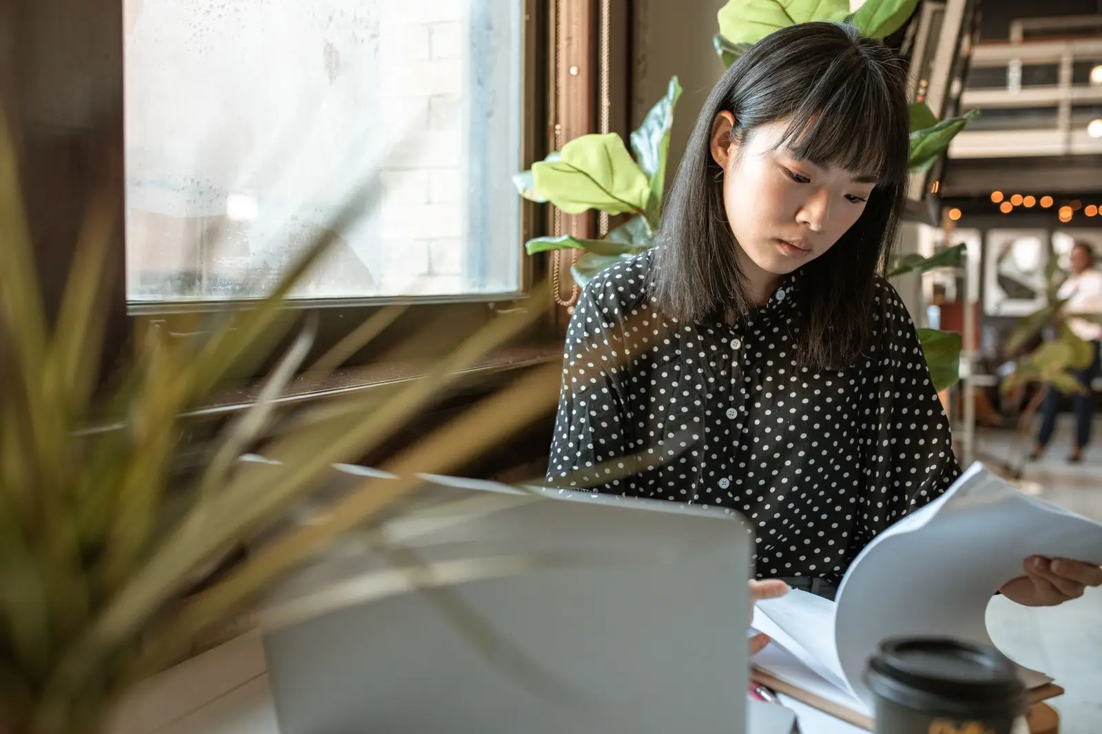 A woman working through papers at a desk beside a laptop