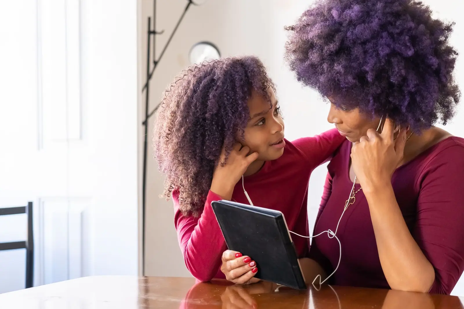 A mother and daughter sharing a tablet with earphones at a table