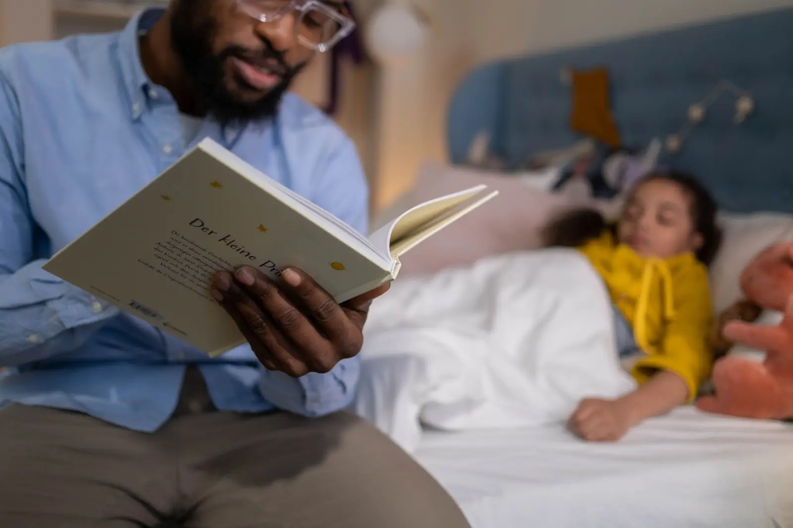 A father reading a bedtime story to his daughter, who is lying in bed