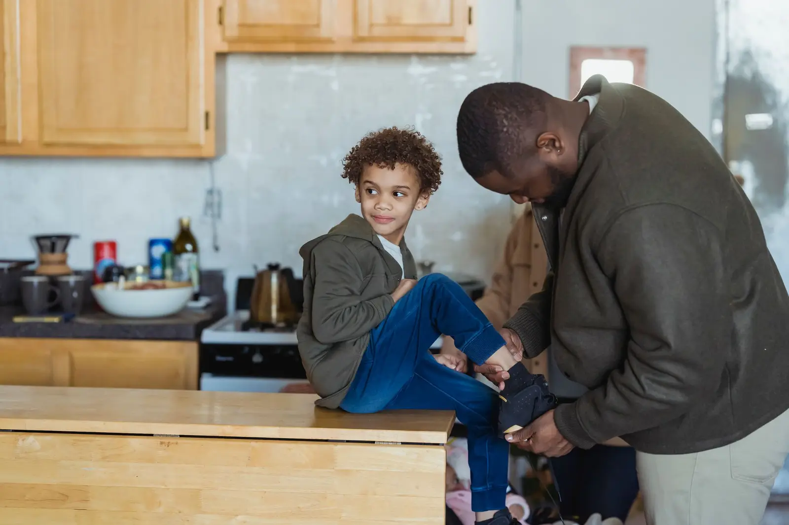 A father helping his son put on his shoes in the kitchen