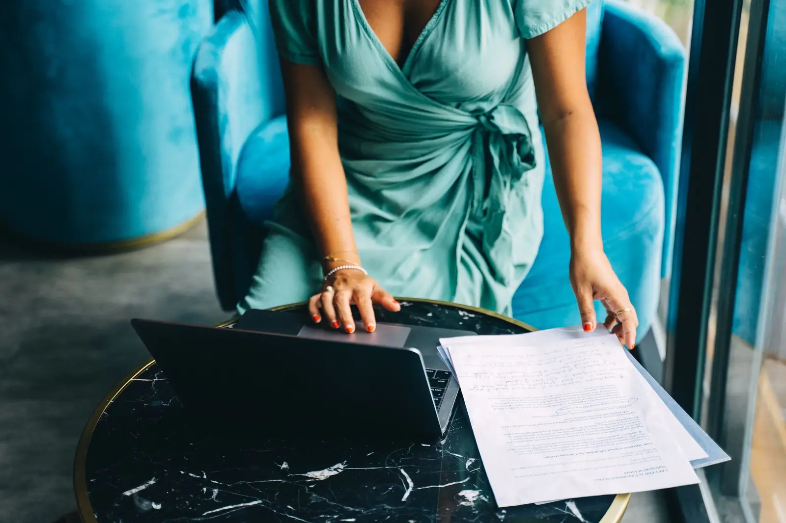 A woman reading documents beside a laptop at a small table