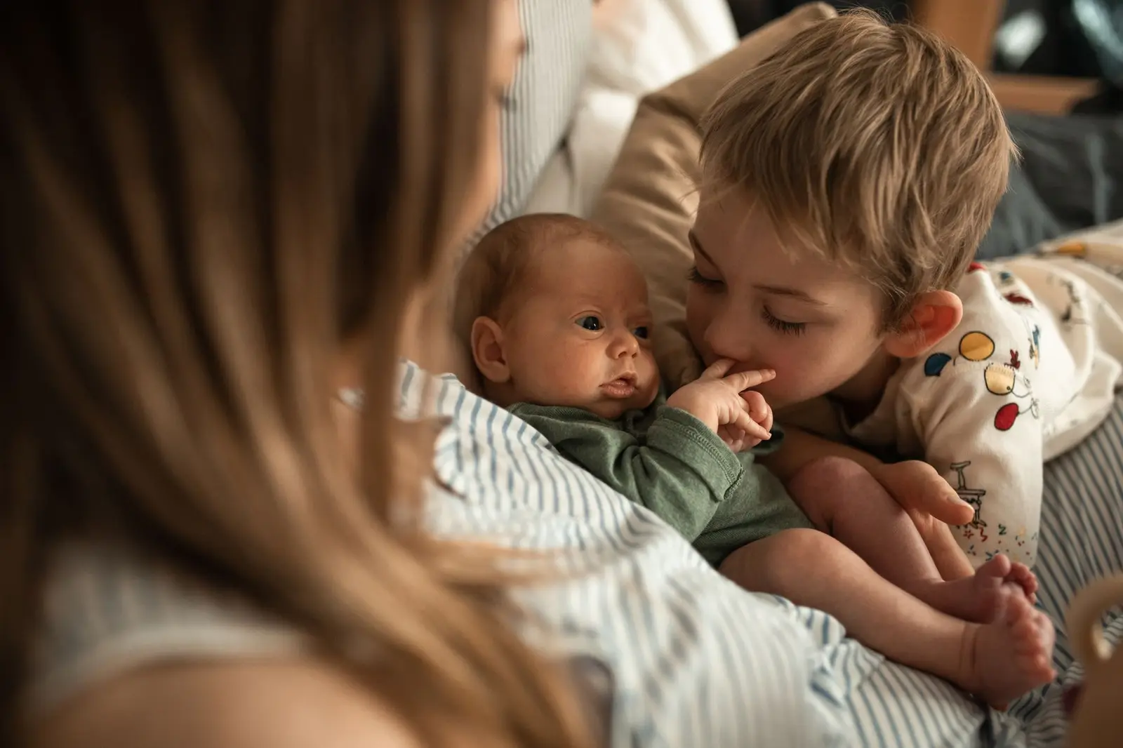 An older child hugging a newborn baby in a parent's arms