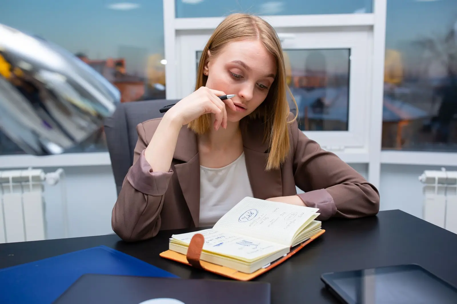 A thoughtful woman sitting at an office desk with a planner