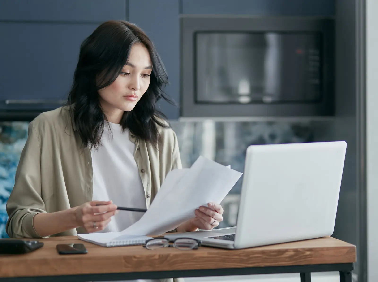 A woman reviewing a document at a laptop in her kitchen