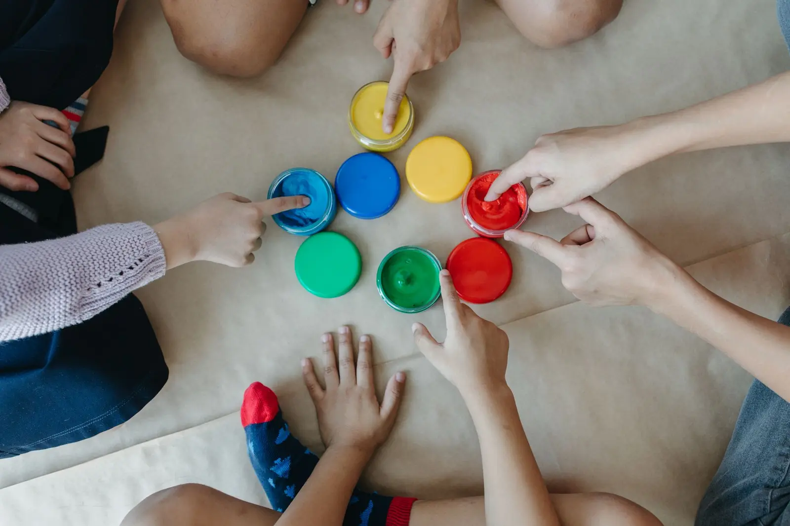 Children's hands reaching into pots of bright paint, seen from above