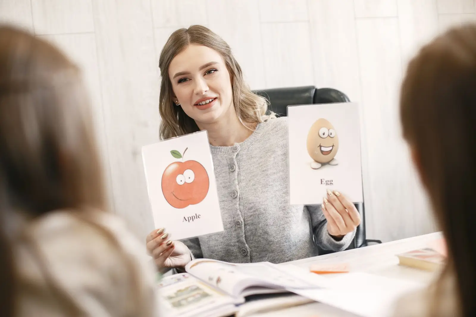 A teacher holding up picture flashcards of an apple and an egg for young students