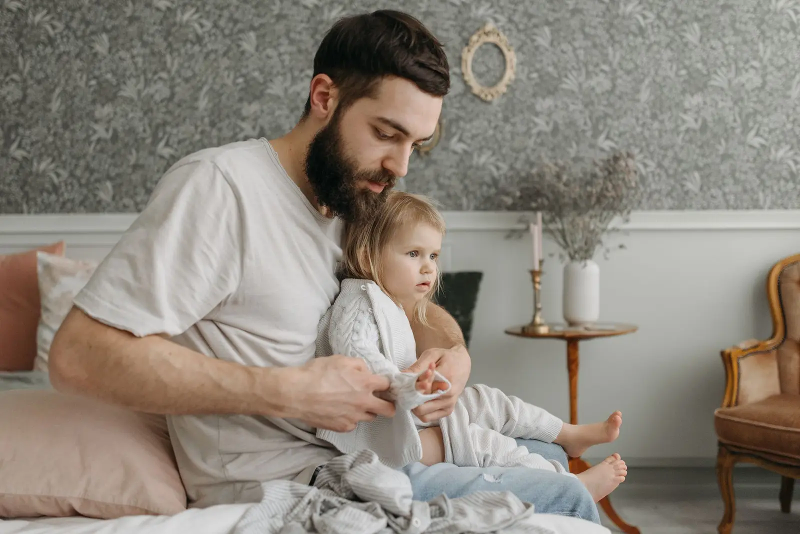 A father helping his young daughter get dressed on a bed