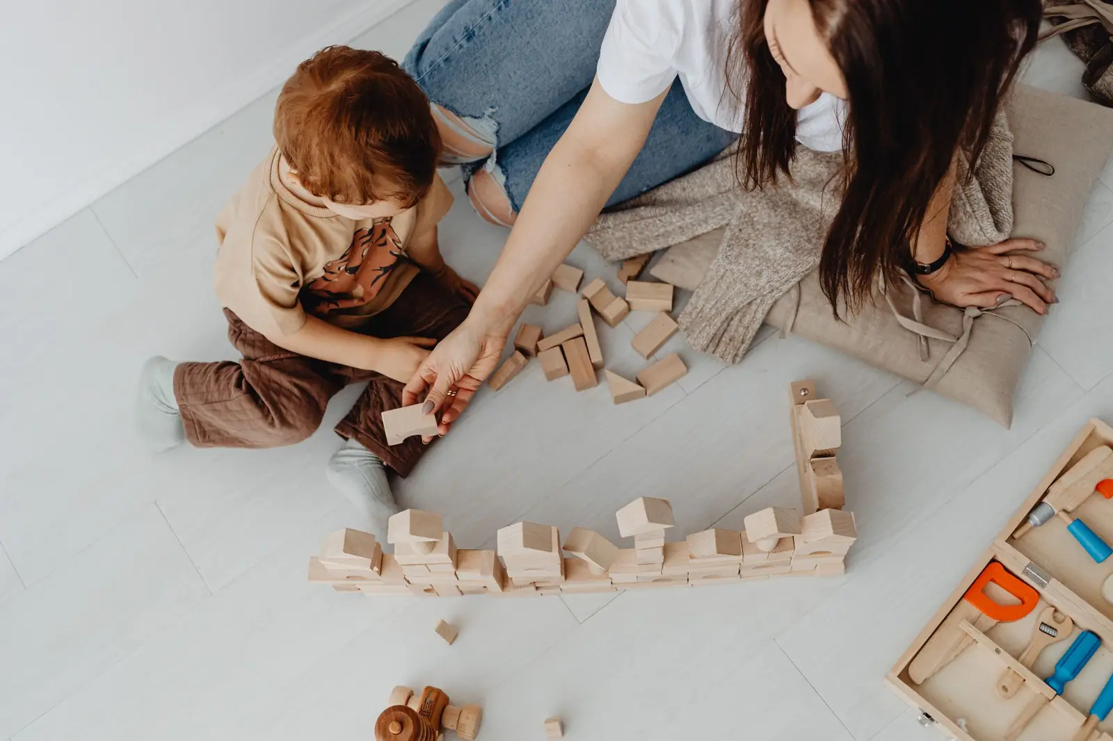 A parent and young child lining up wooden blocks together on the floor