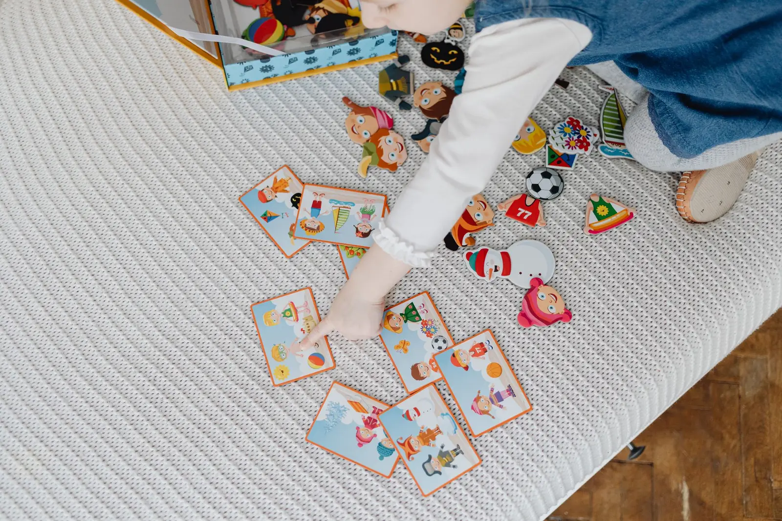 A child arranging picture cards and stickers on a bed, seen from above