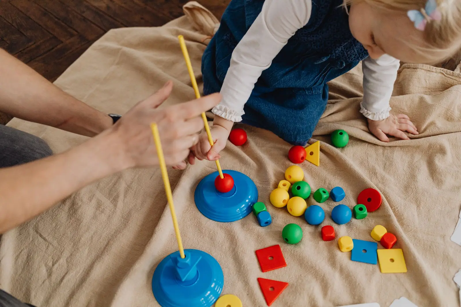 A child playing with colorful shape toys while an adult guides the activity