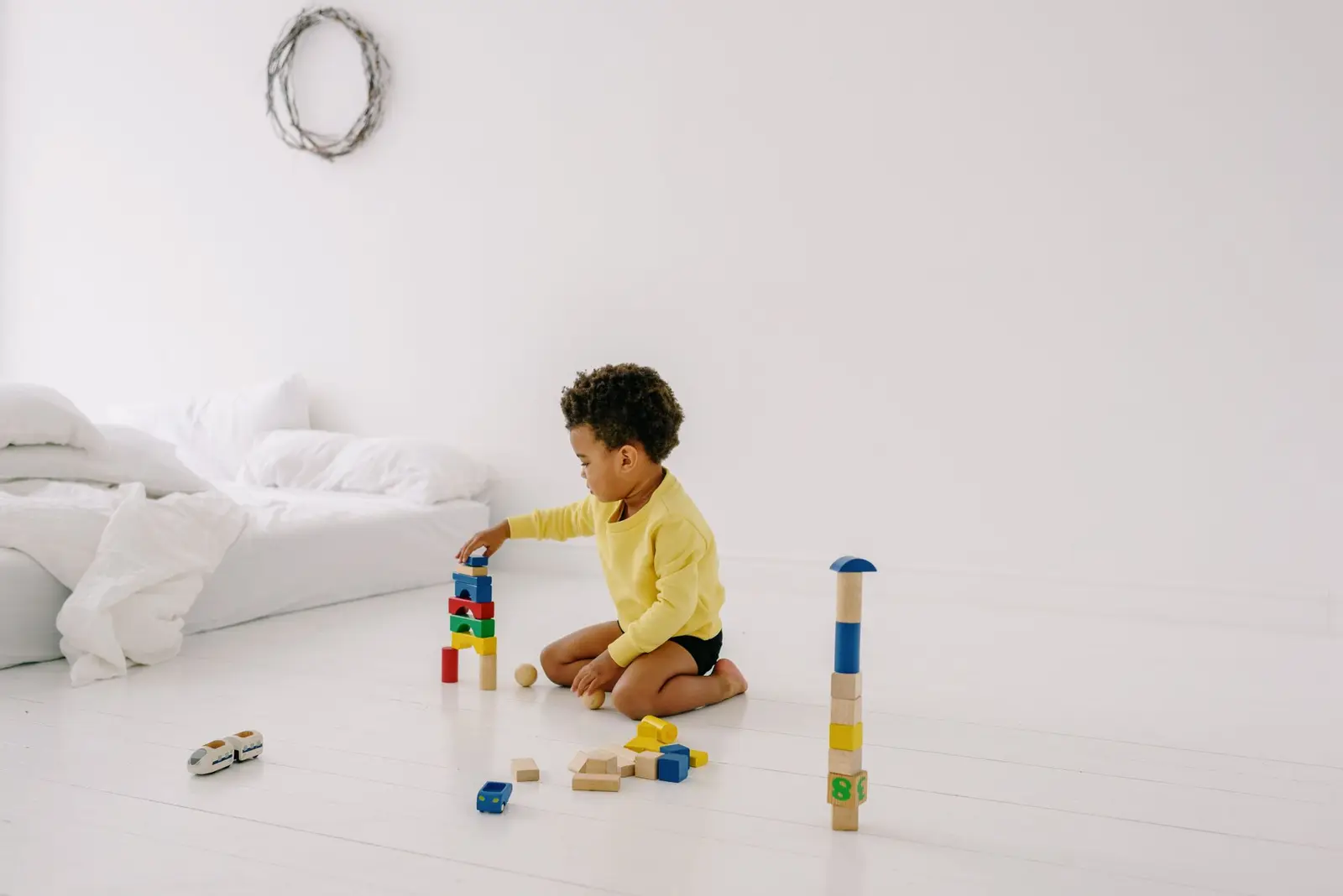 A young child building towers with wooden blocks on a white floor