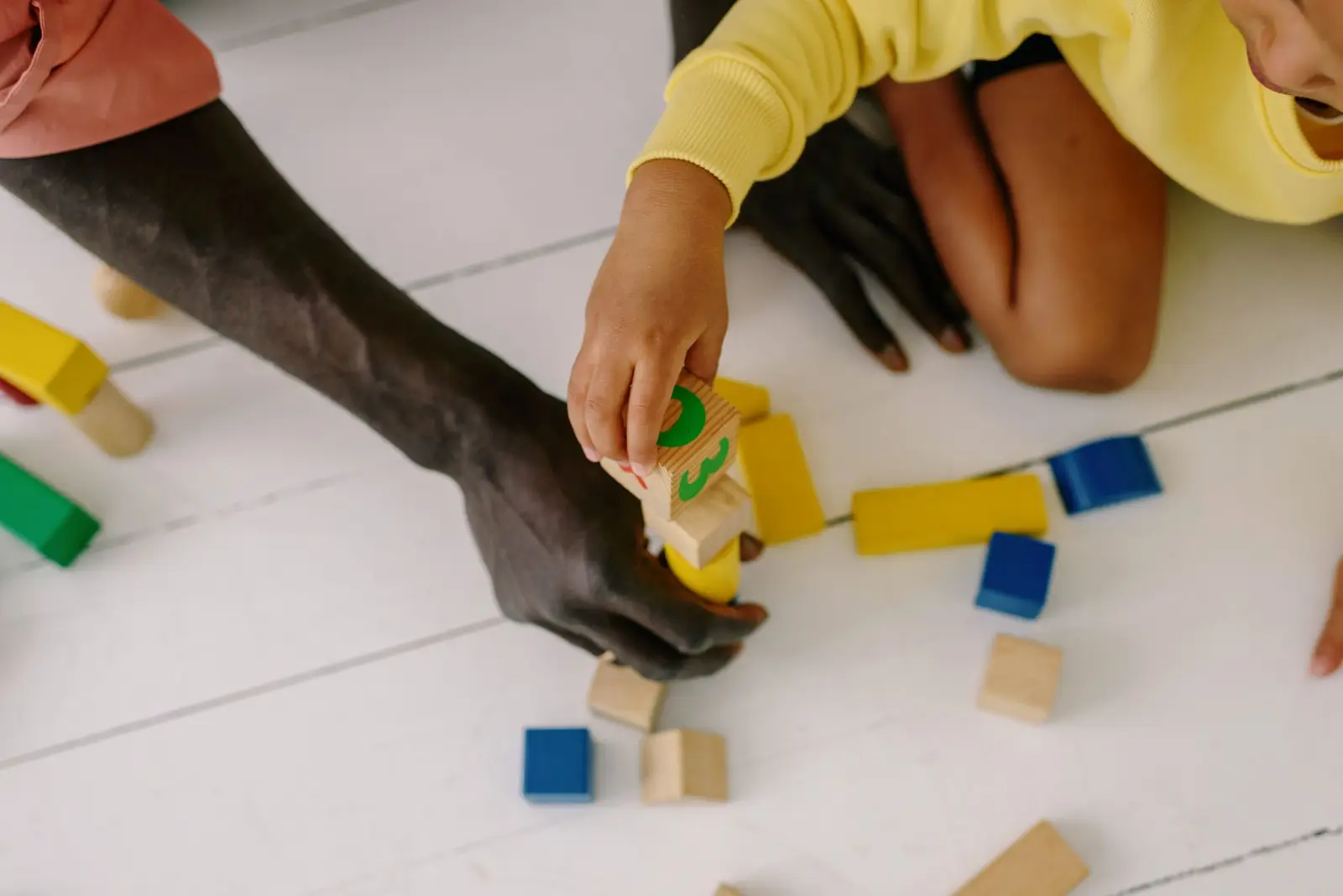 An adult and a child building with colourful wooden blocks on the floor