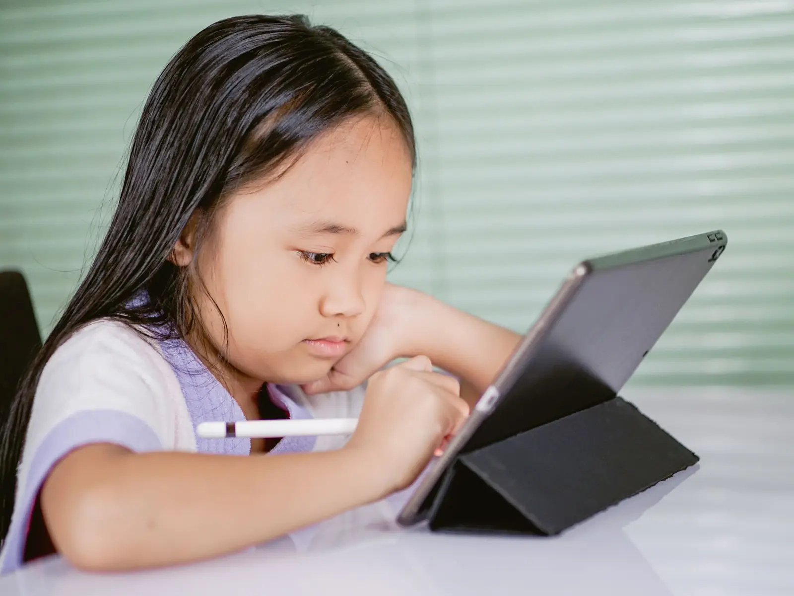A girl concentrating on a tablet with a stylus at a table