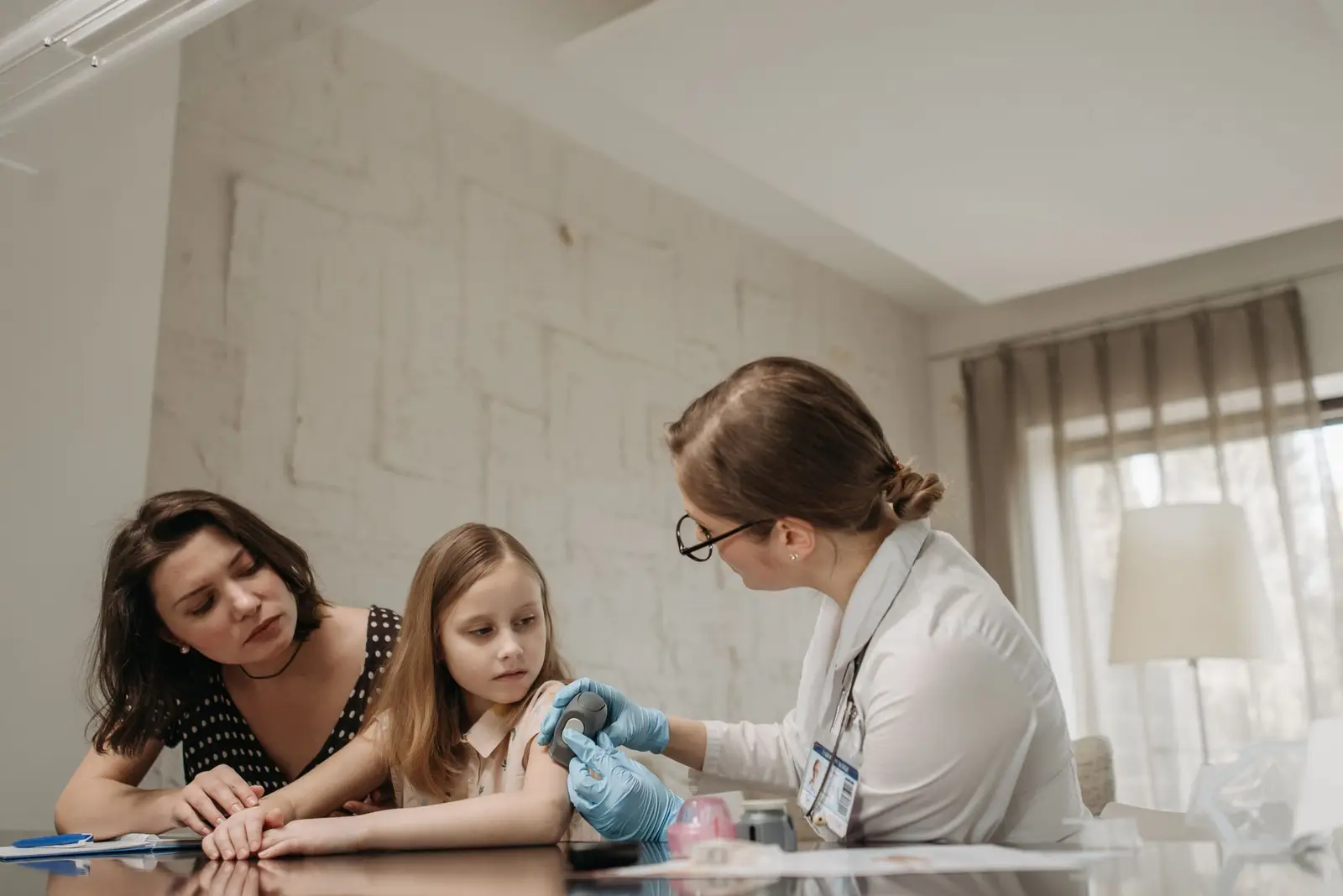 A mother sitting with her daughter while a doctor checks the girl's arm at a desk