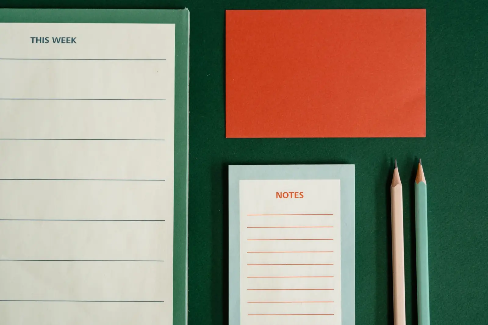 A weekly planner sheet, notepad and pencils on a green surface