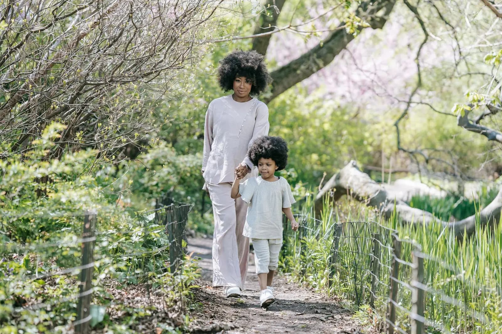 A mother and daughter walking hand in hand along a green path