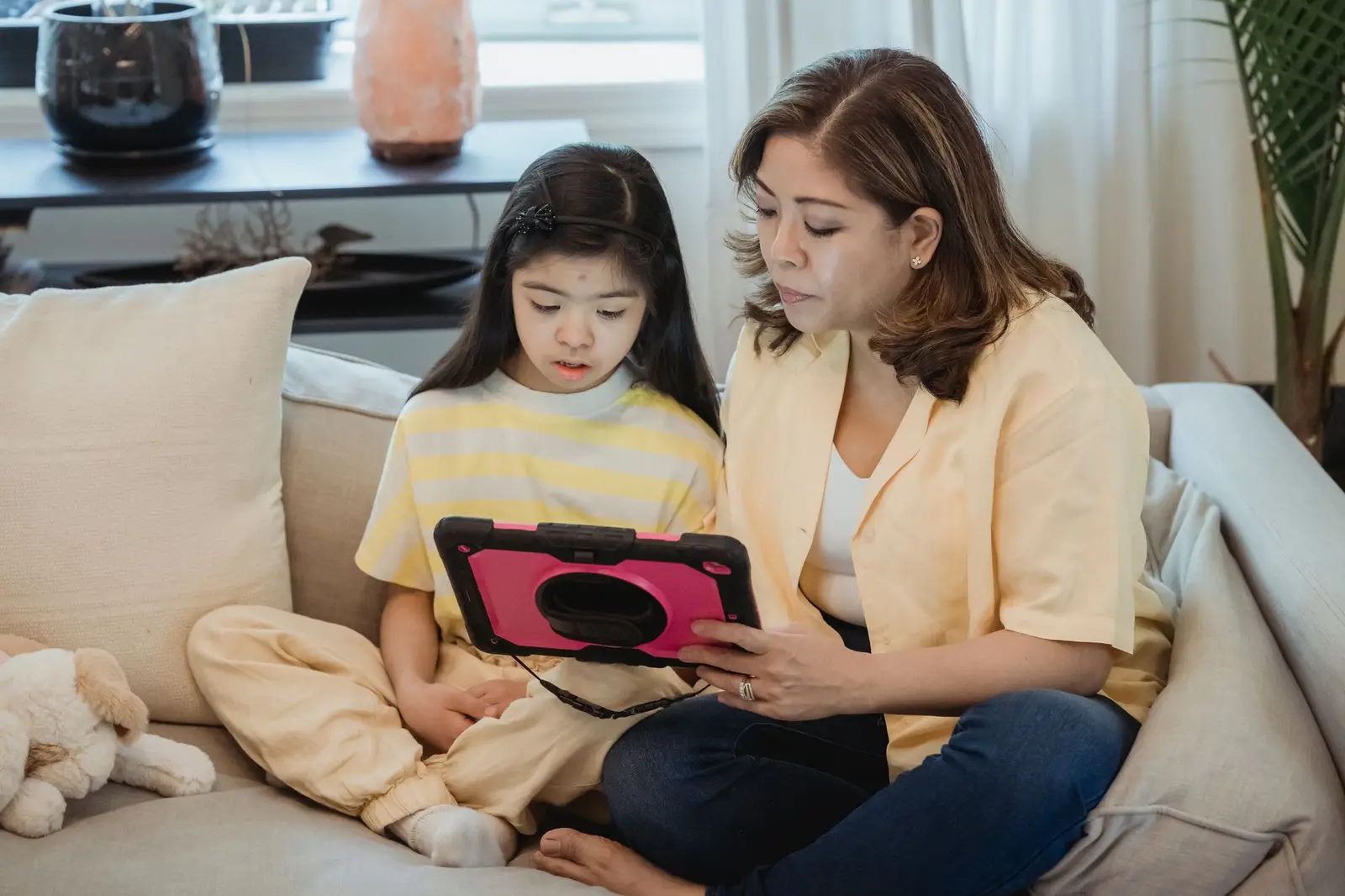 A mother and daughter using a tablet together on the sofa