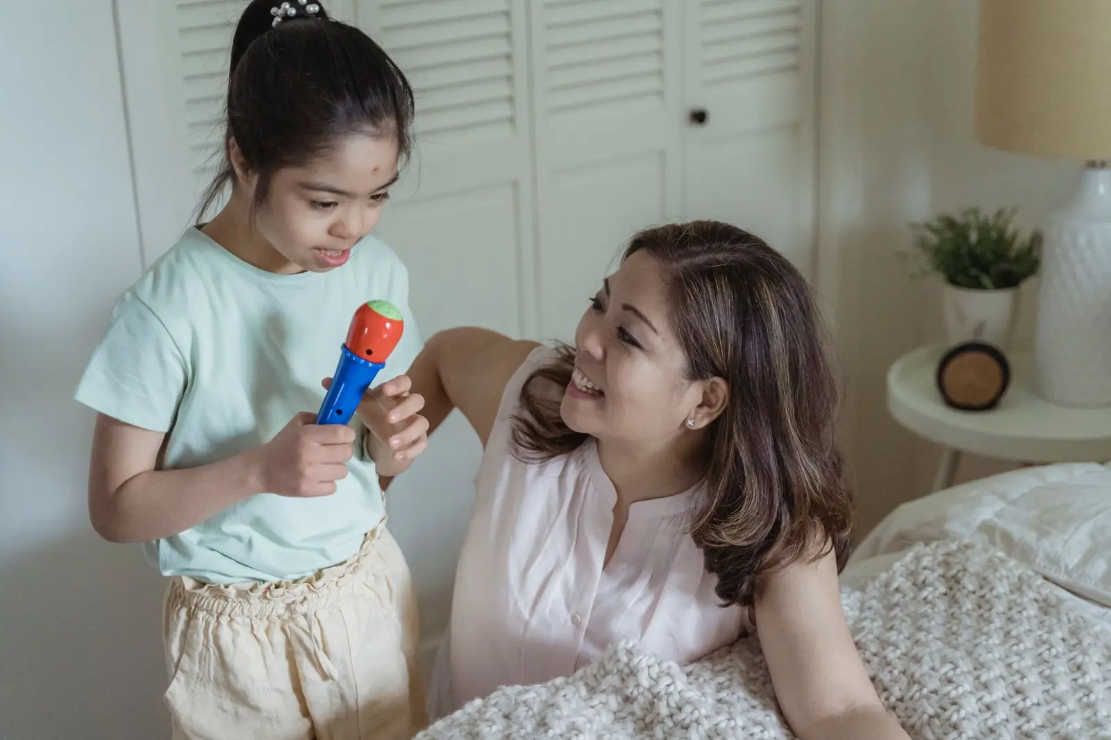 A mother smiling as her daughter talks into a toy microphone