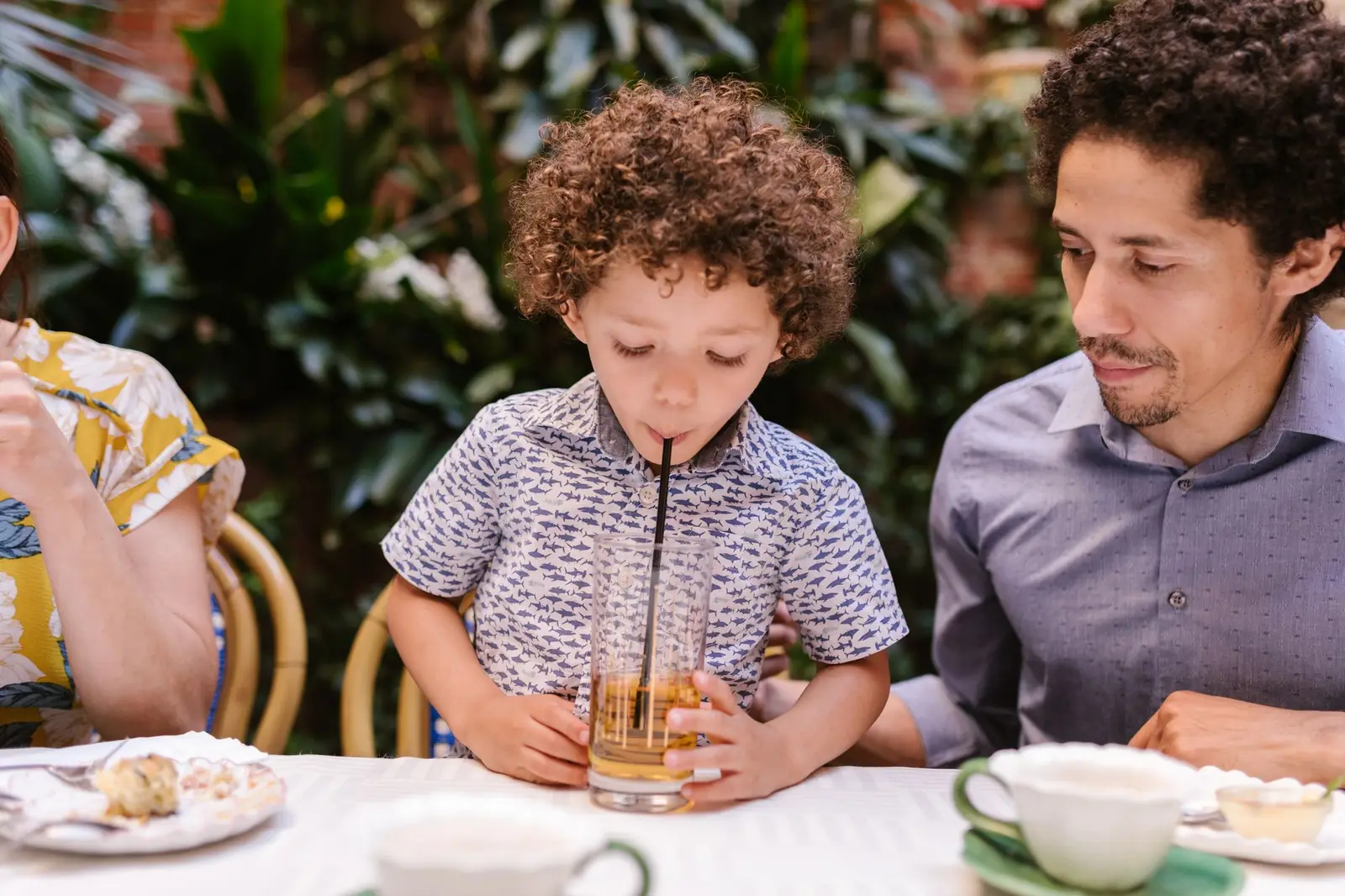 A boy sipping a drink through a straw next to his father at a café table