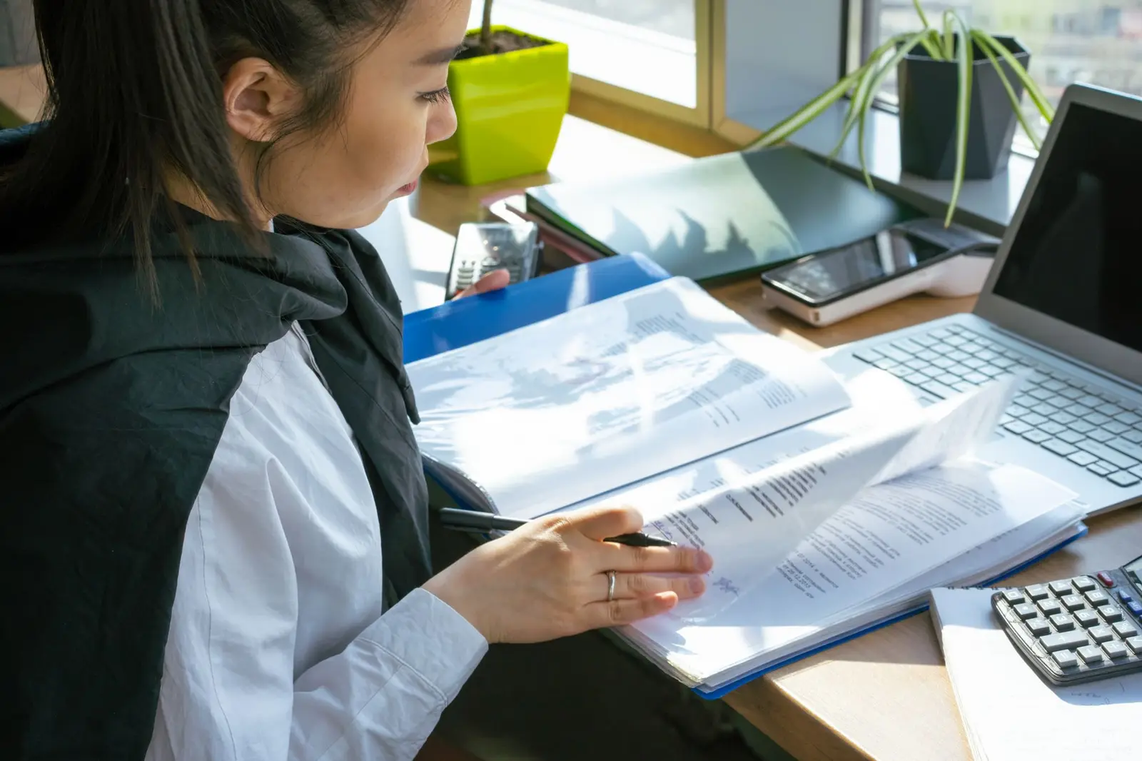 A person working through papers at a desk with a laptop and calculator