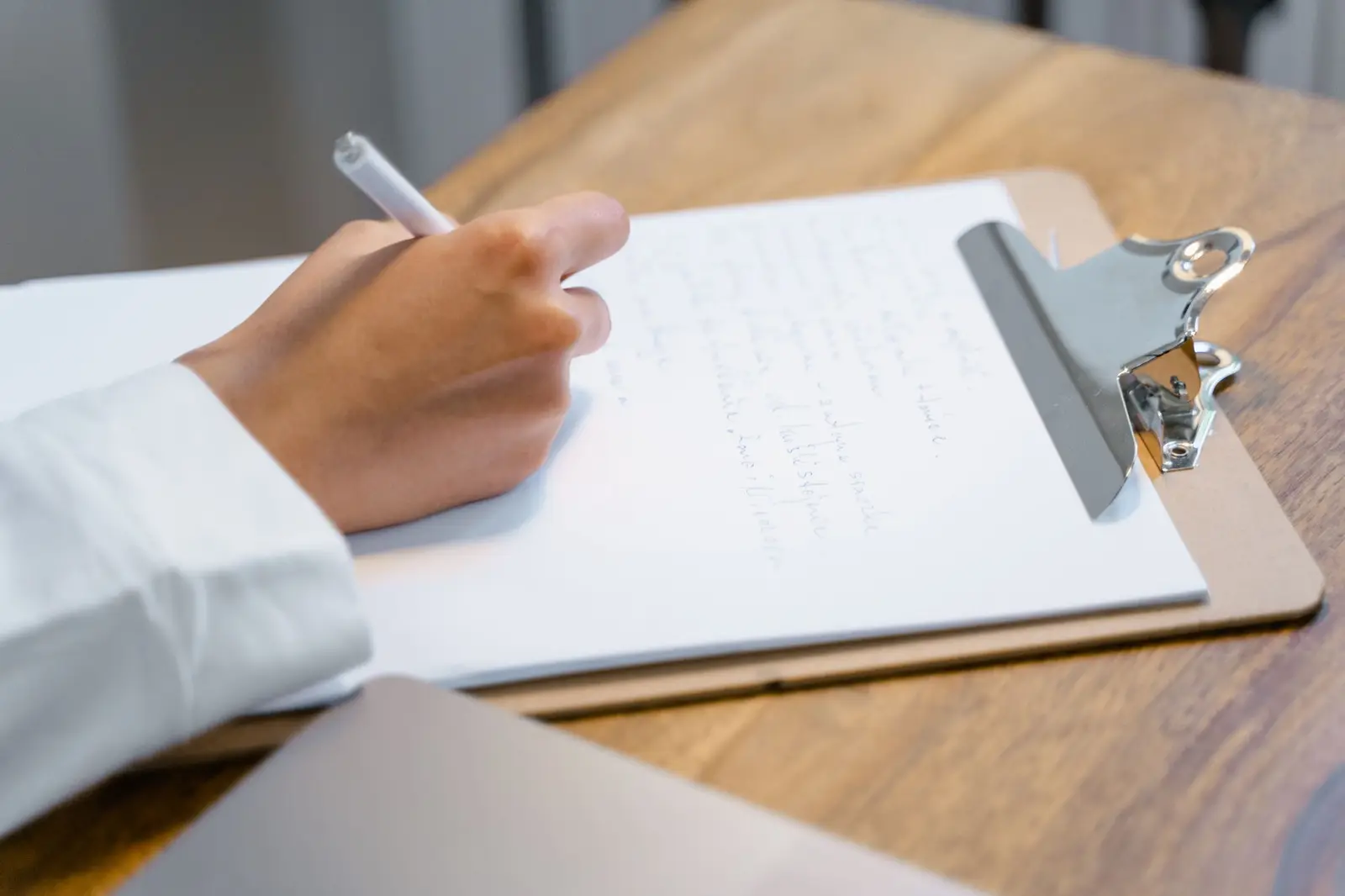 A hand writing notes on a clipboard at a wooden table