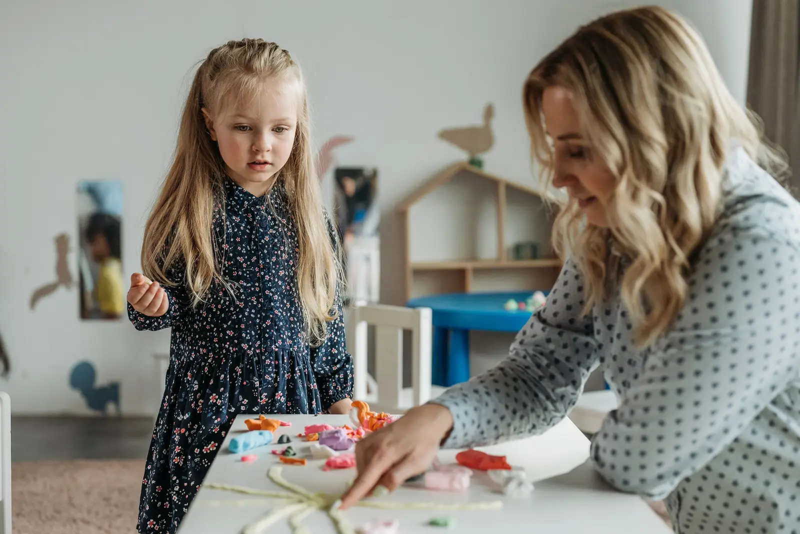 A woman and a young girl working on a craft activity in a bright playroom