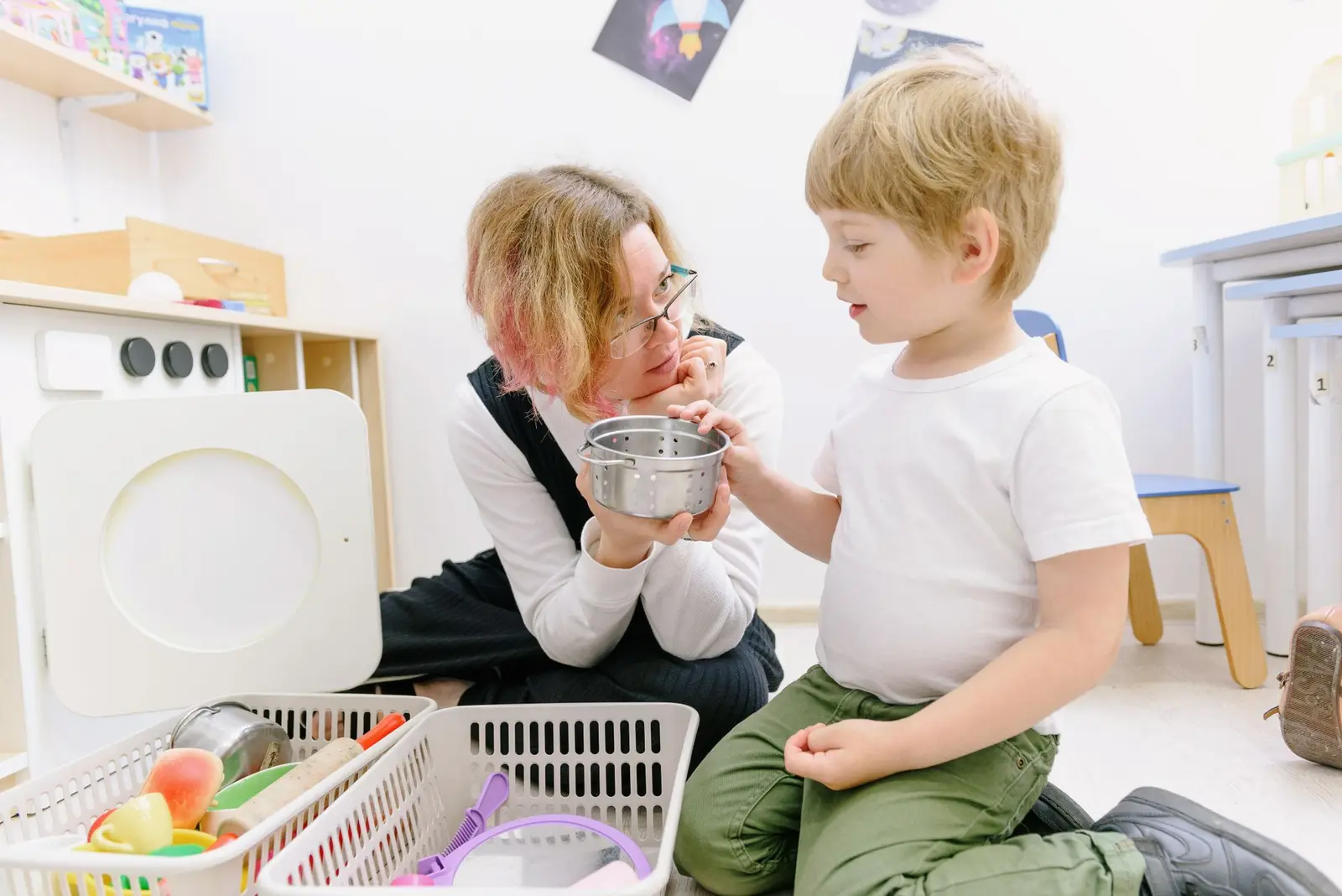A teacher and a young boy playing with a toy kitchen in a playroom