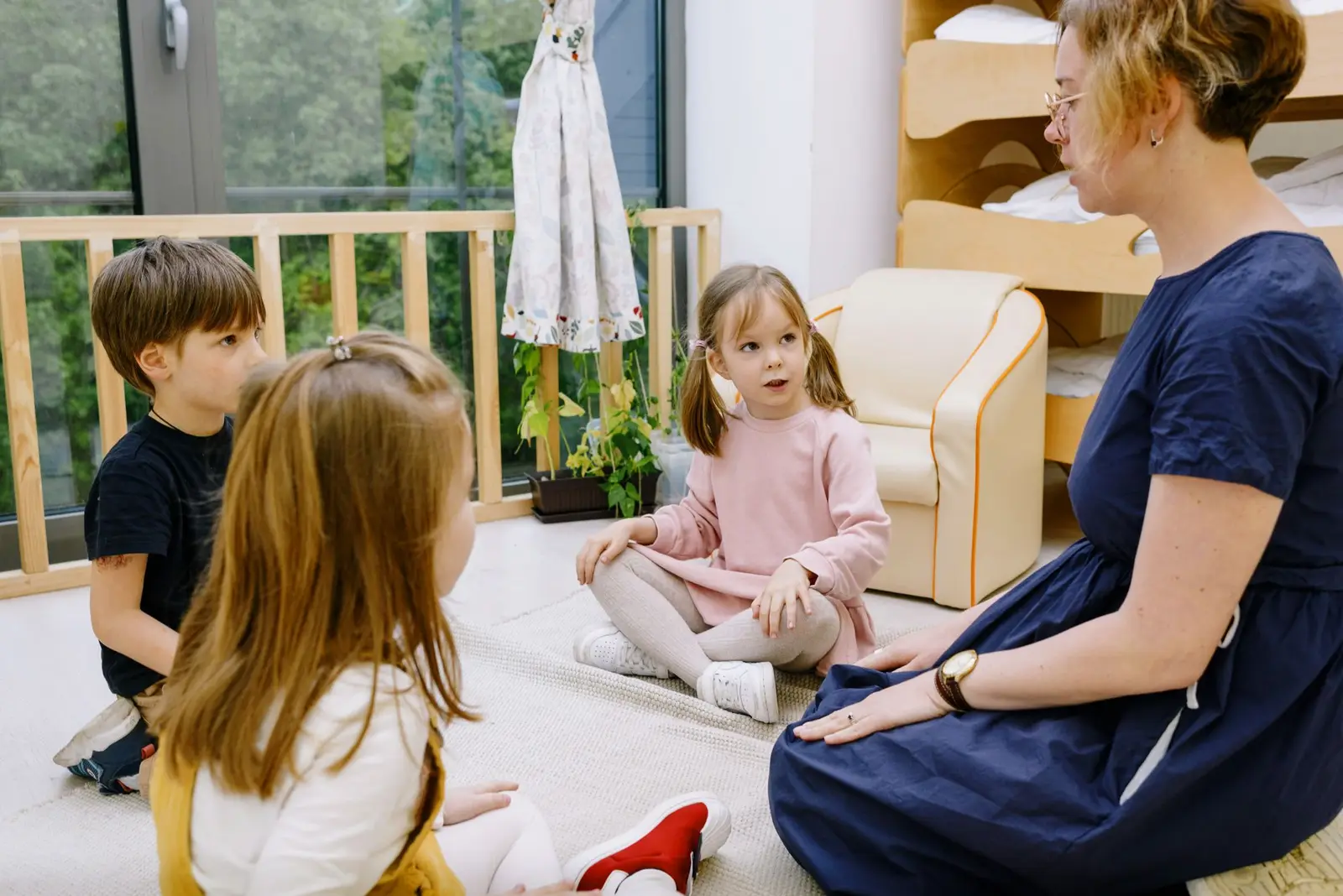 A teacher sitting on the floor with young children in a bright nursery room