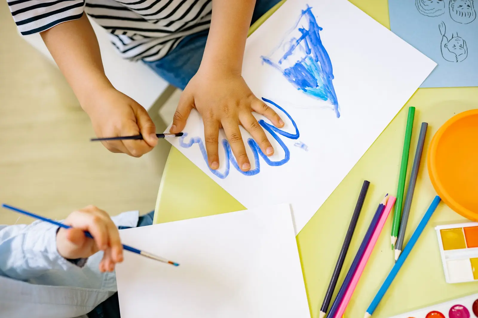 Children painting with watercolors and colored pencils at a table