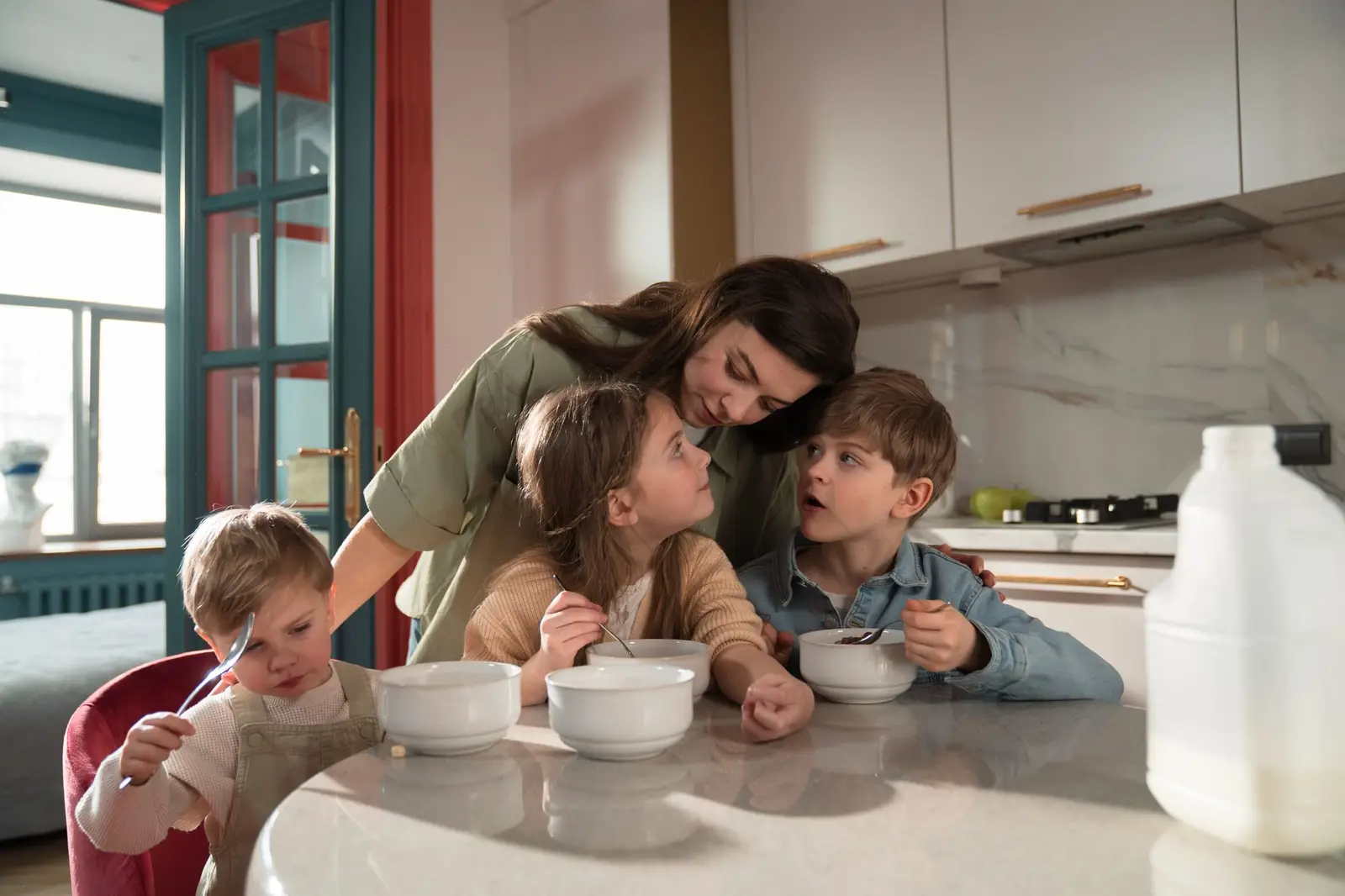 A mother and three children eating breakfast together at the kitchen counter
