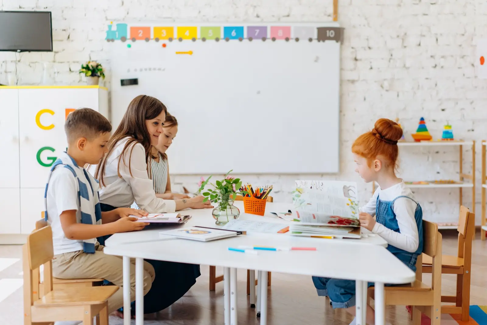 Pupils working at a table with their teacher in a bright, colourful classroom
