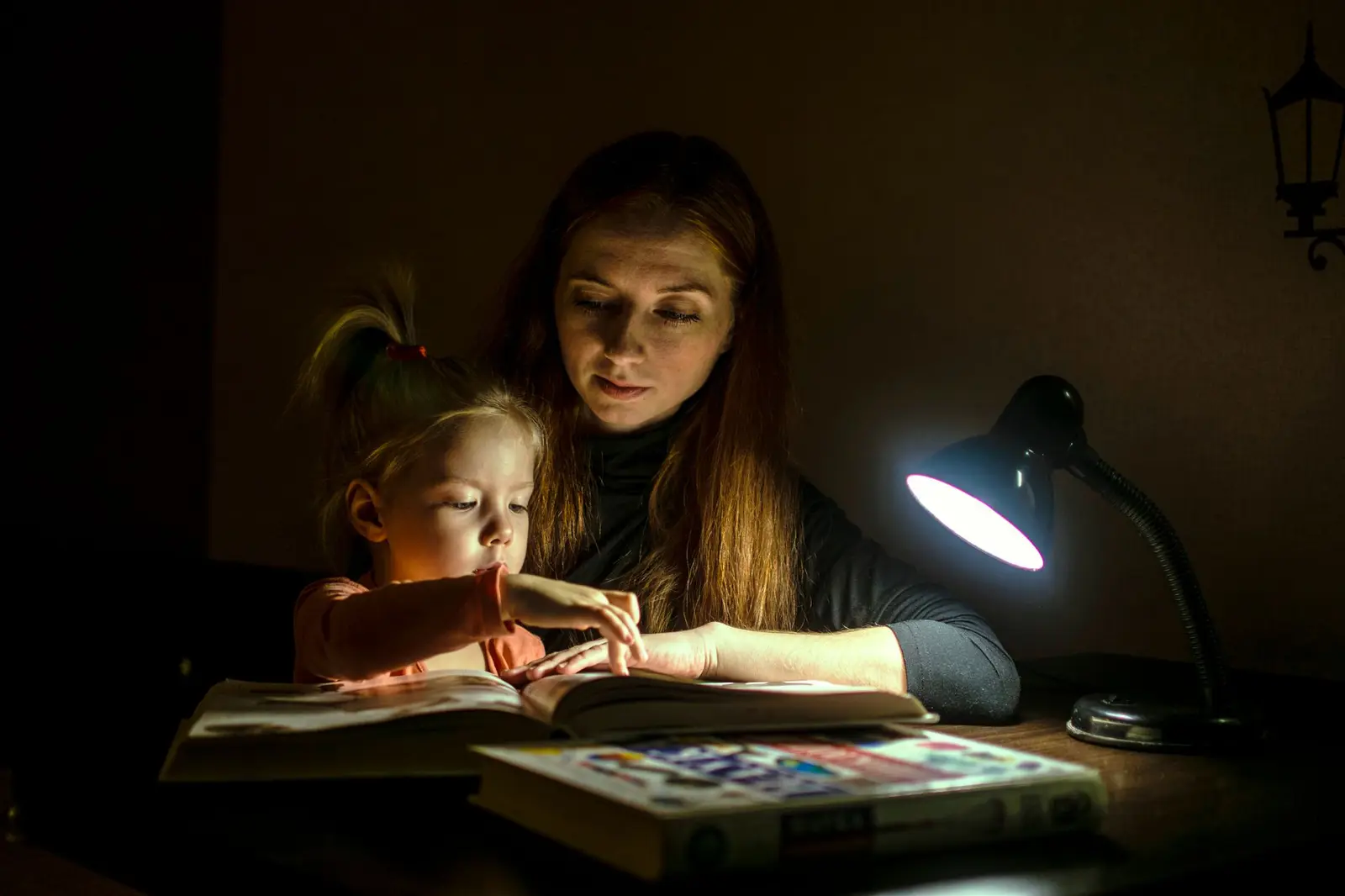 A mother and daughter reading a book together under a lamp