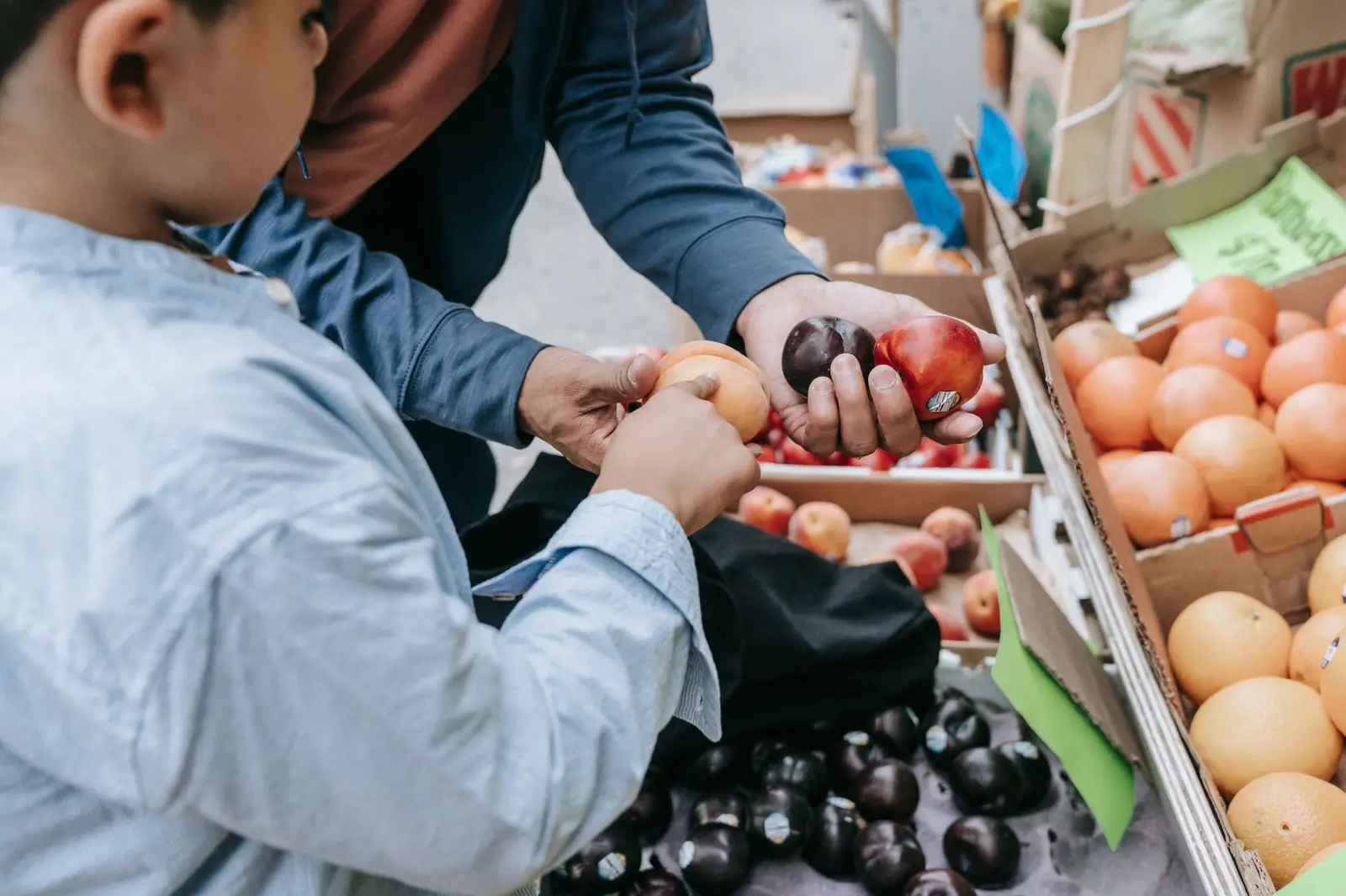 A boy and his father choosing fruit at a market stall